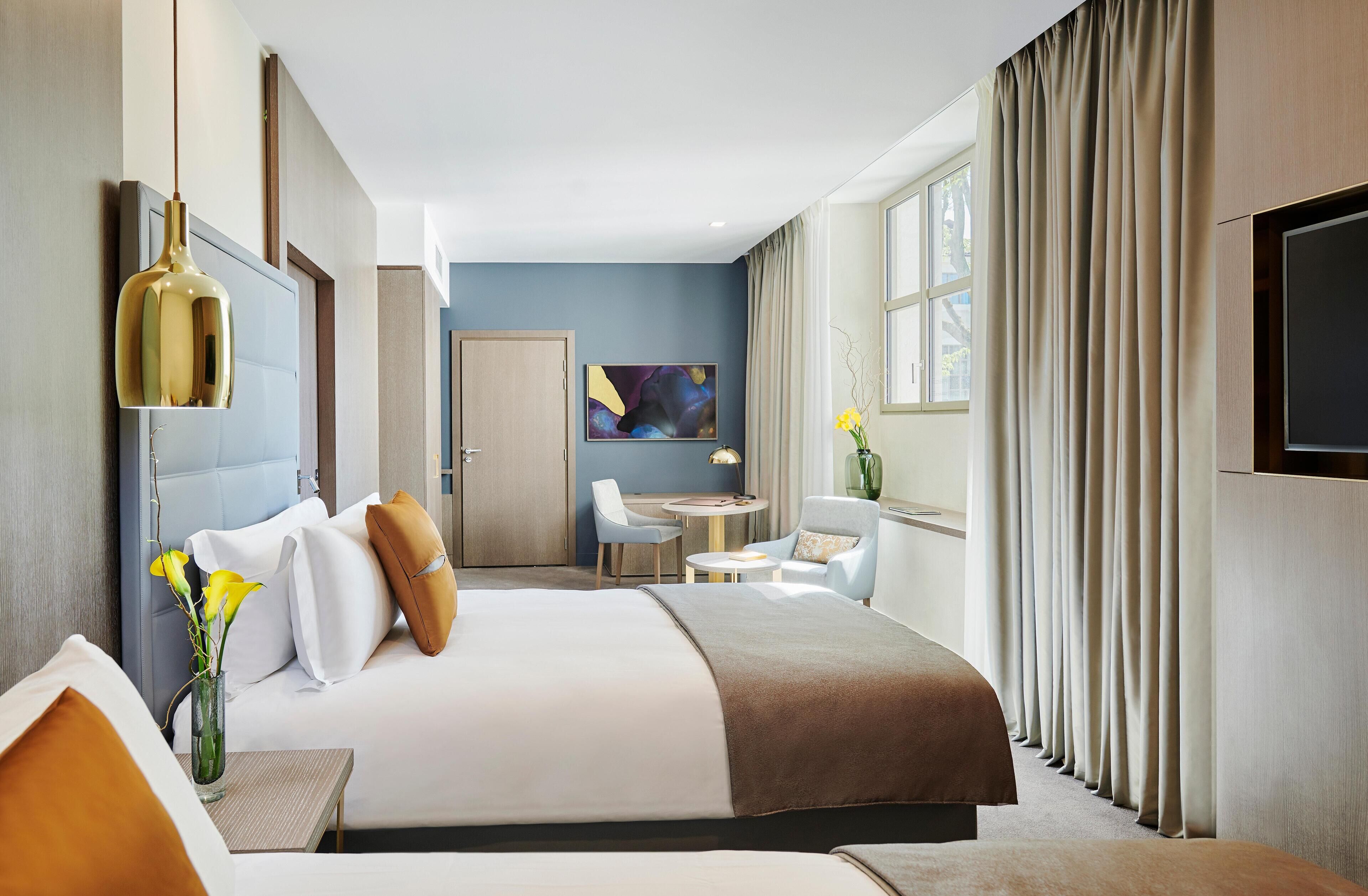 A modern hotel room with a large bed, a desk, a chair, a TV, and a window with curtains.