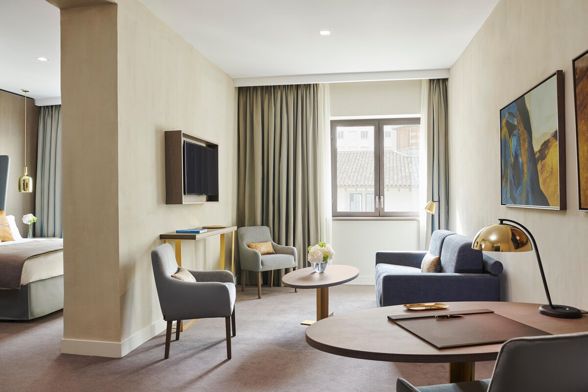 Una habitación de hotel con una cama, dos sillones, un sofá, una mesita y un televisor.