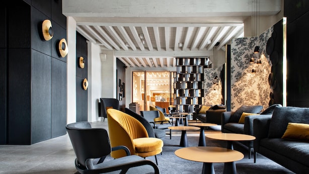 Una sala de estar moderna con un sofá, sillones y una mesa de centro. Hay una estantería y una pared decorativa con diseños circulares.