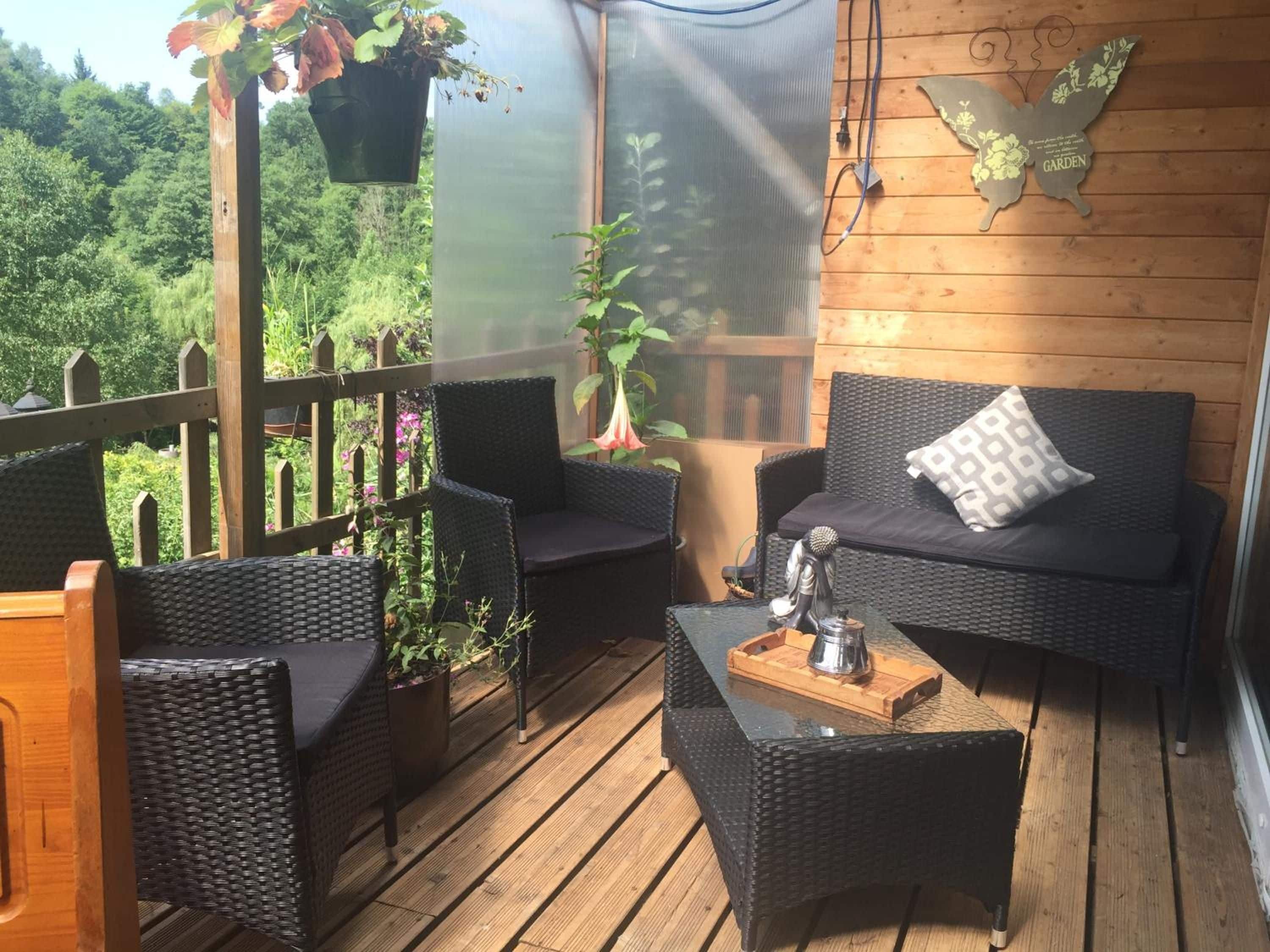 A covered outdoor seating area with wicker furniture and a view of a lush garden.