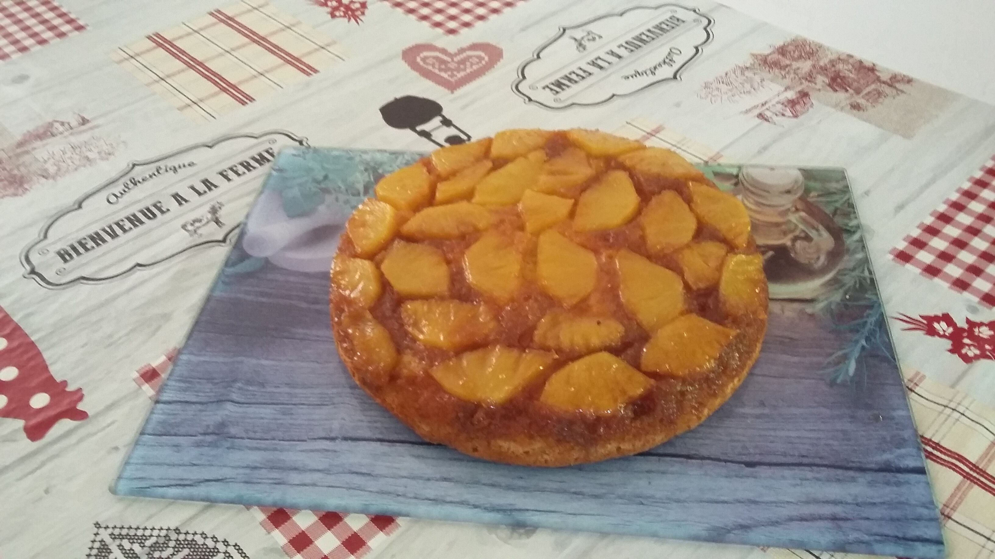 Una tarta redonda de frutas sobre un paño azul, colocada en una mesa con mantel a cuadros.