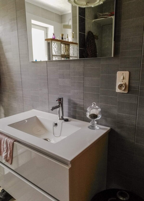 A bathroom with a white sink, a mirror, and grey tiled walls.