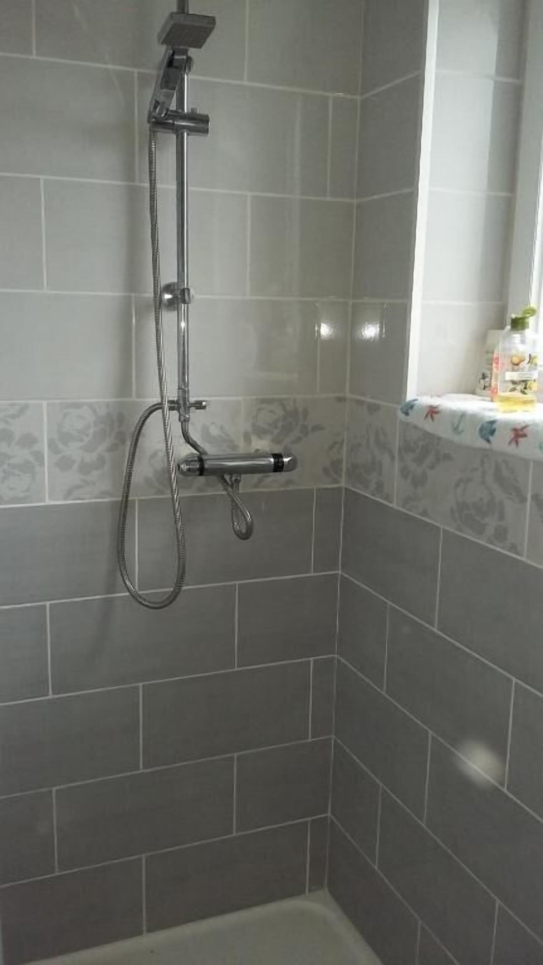 Un espacio de ducha con azulejos grises y un cabezal de ducha manual.