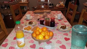 A dining table with a heart-patterned tablecloth, various food items, and a bottle of orange juice. - La Chti Cabane (Taintrux)