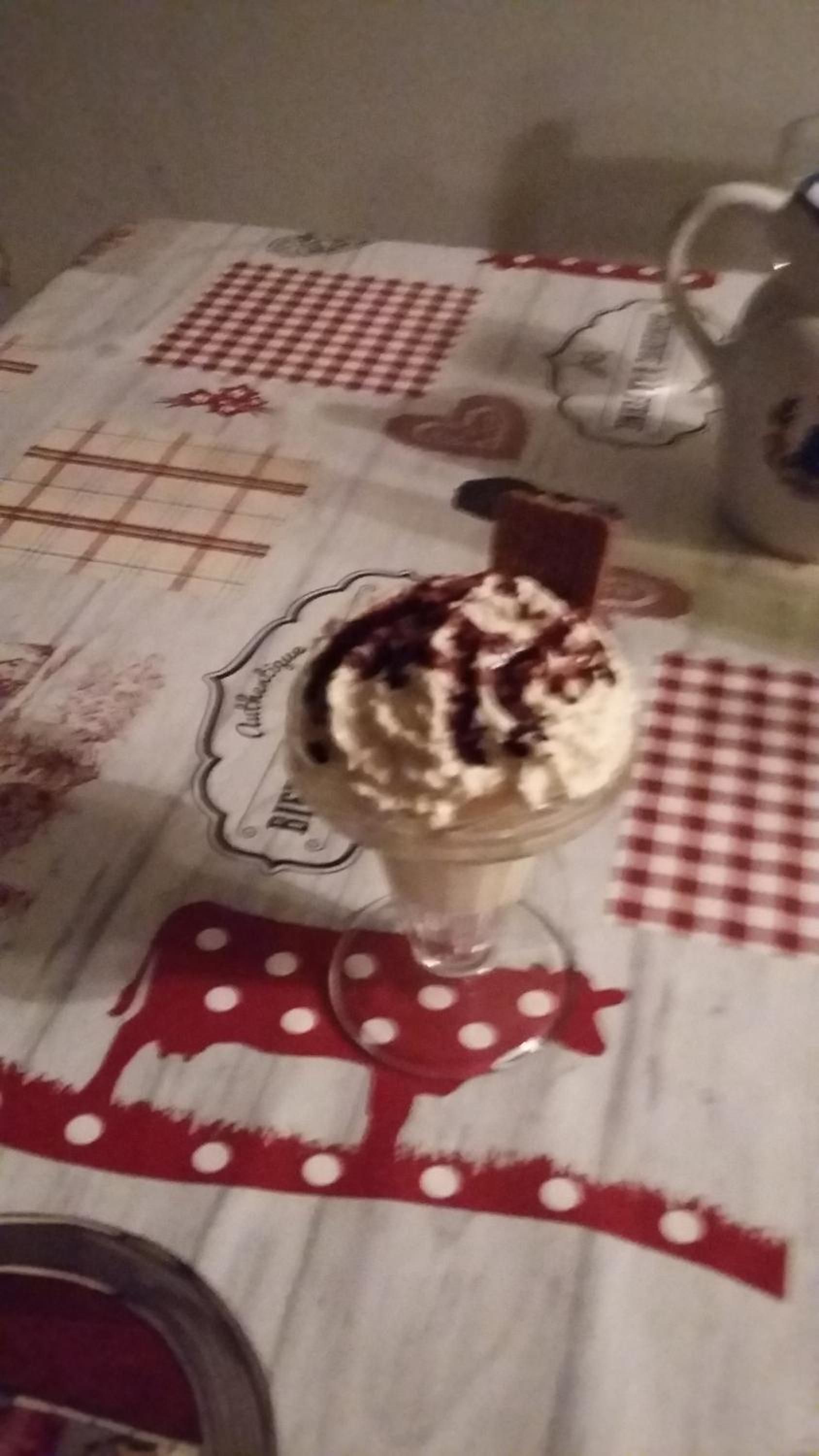A dessert on a table with a checkered tablecloth, a glass, and a teapot.