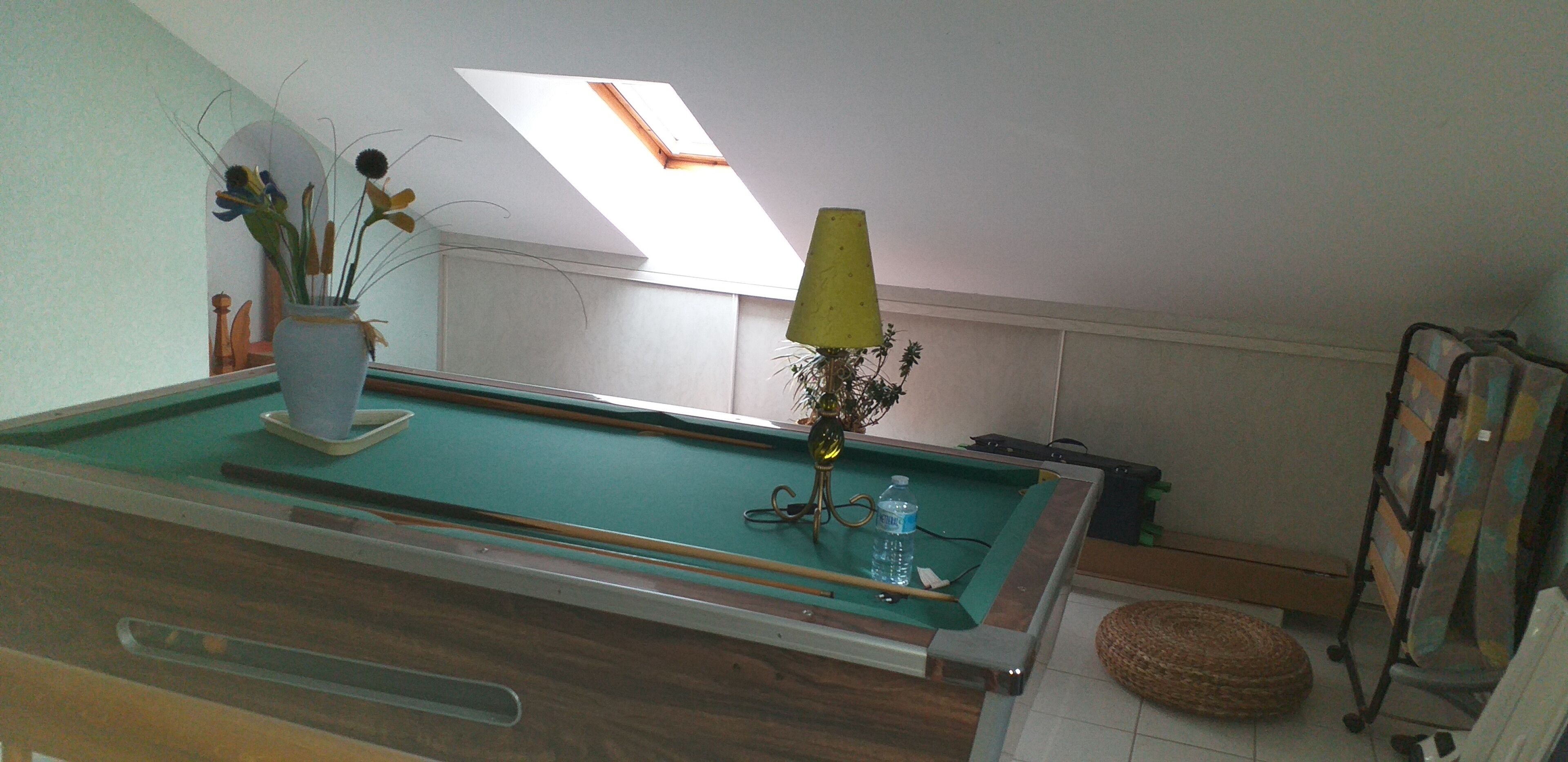 Une table de billard avec un vase de fleurs, une lampe et une bouteille d’eau.
