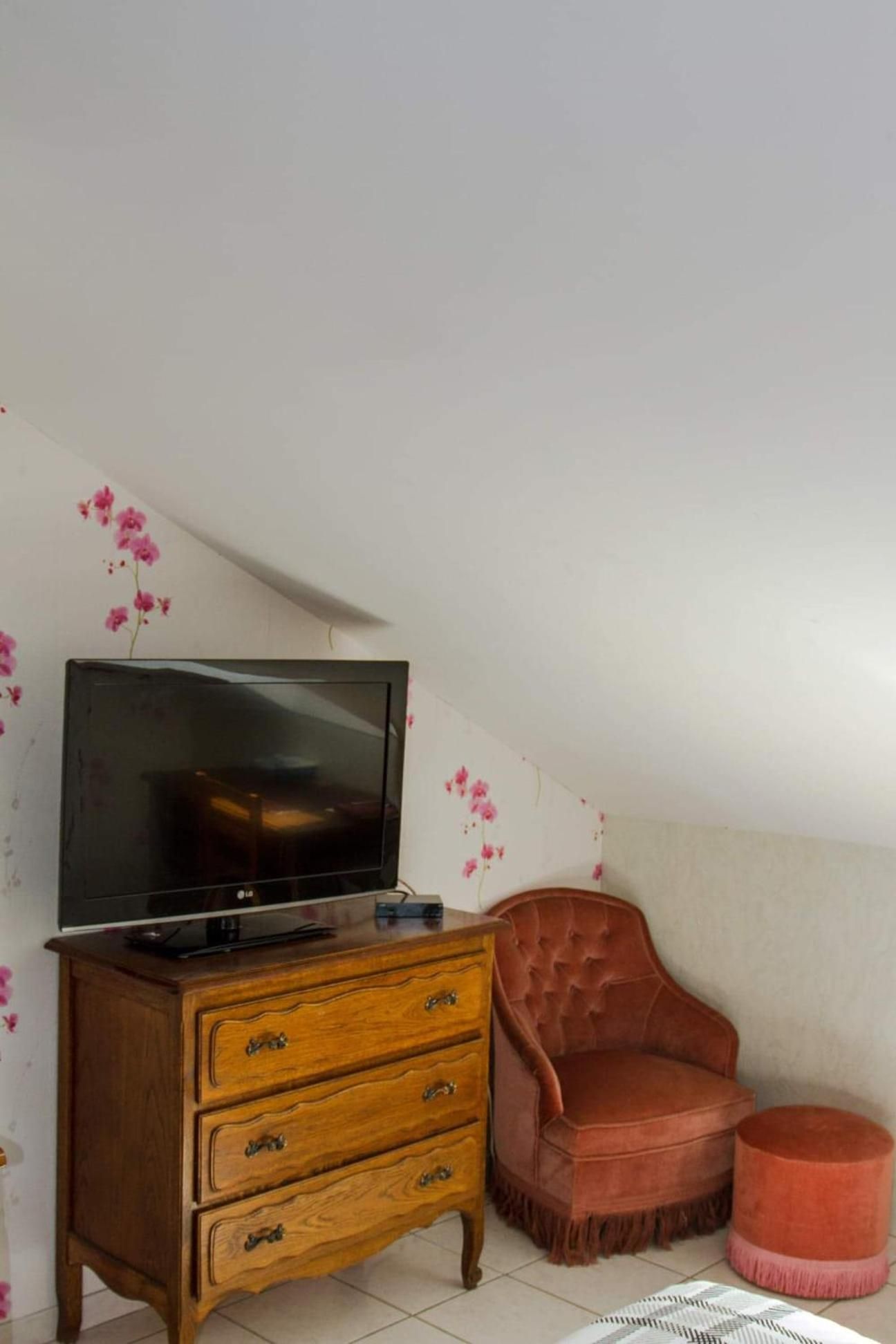 A room with a television on a wooden dresser, a red chair, and a small ottoman.