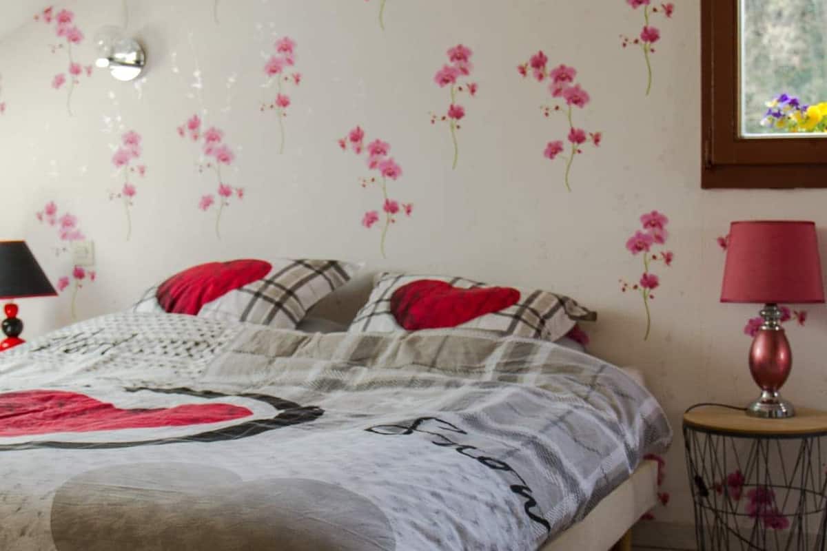 A bedroom with a bed, pillows, a bedside lamp, and a wall with floral wallpaper.