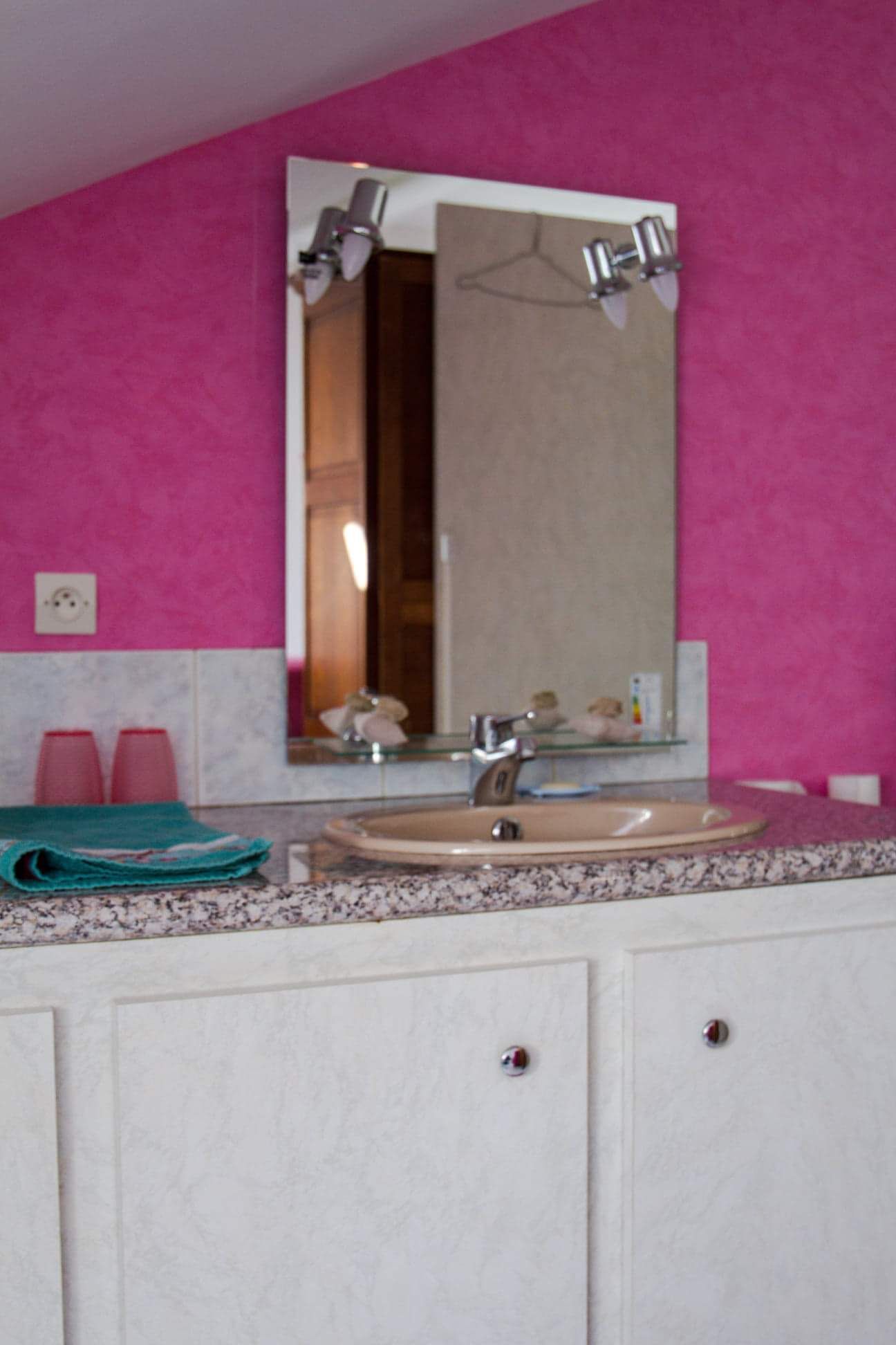 Ein Badezimmer mit einer rosafarbenen Wand, einem Waschbecken mit Spiegel darüber und zwei roten Tassen auf der Ablagefläche.