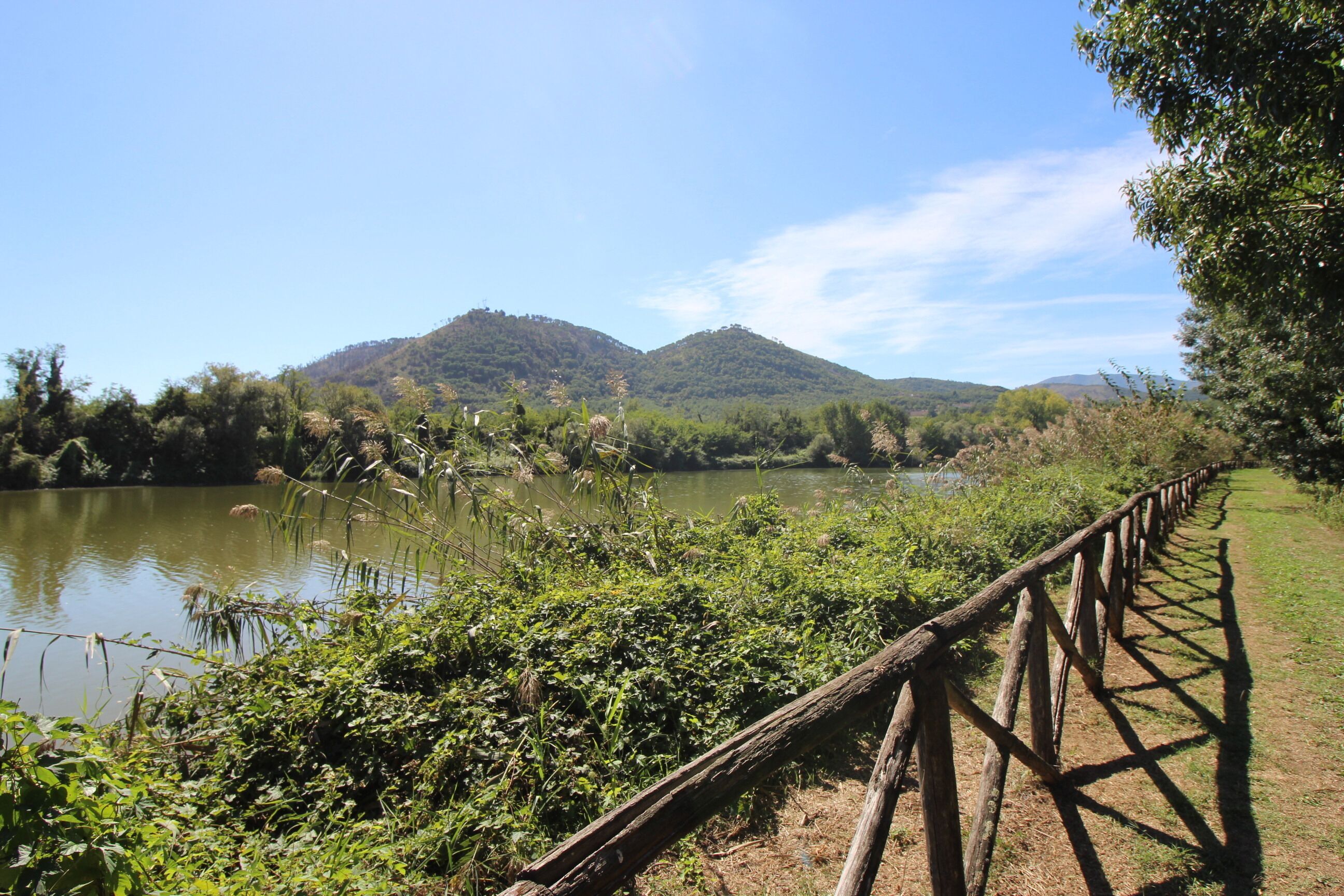 A wooden fence along a riverbank with lush greenery and hills in the background.