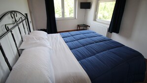Un dormitorio con cama, televisor montado en la pared y ventana con cortinas.