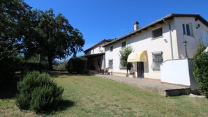 Una casa de dos pisos con un patio, un pequeño jardín y un cielo azul despejado.