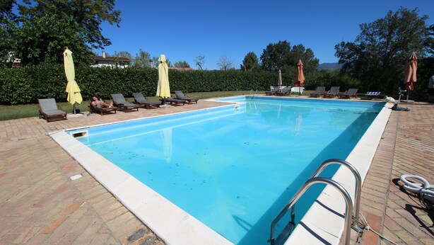 Una piscina rectangular con superficie de agua azul cristalina, rodeada por un solado de baldosas.