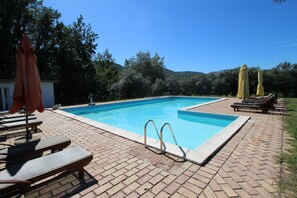 Une piscine rectangulaire bordée d’une terrasse en briques, entourée de chaises longues et de parasols.