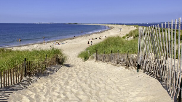 Ein Sandstrand mit einer Holzzaun und freiem Blick auf das Meer.