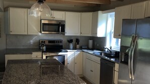 Eine Küche mit Granit Arbeitsplatten, weißen Schränken, Edelstahlgeräten und einer Holzbalkendecke.