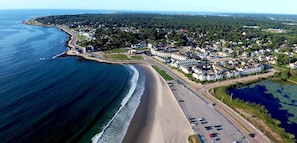 Vista aérea de un pueblo costero con playa, puerto deportivo y zonas residenciales.