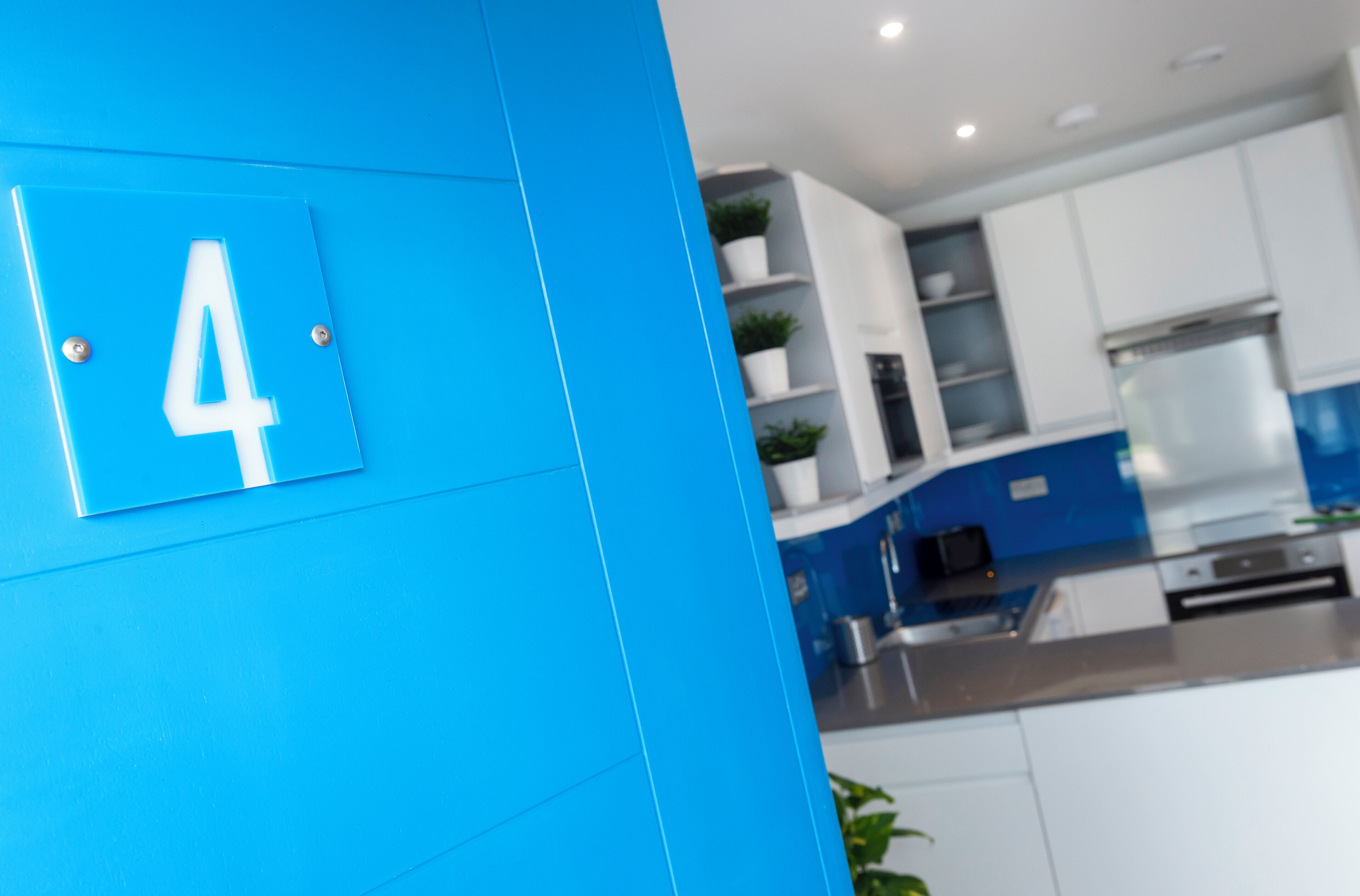 Een moderne keuken met witte kasten, een blauwe accentmuur en een bord met het getal '4'.