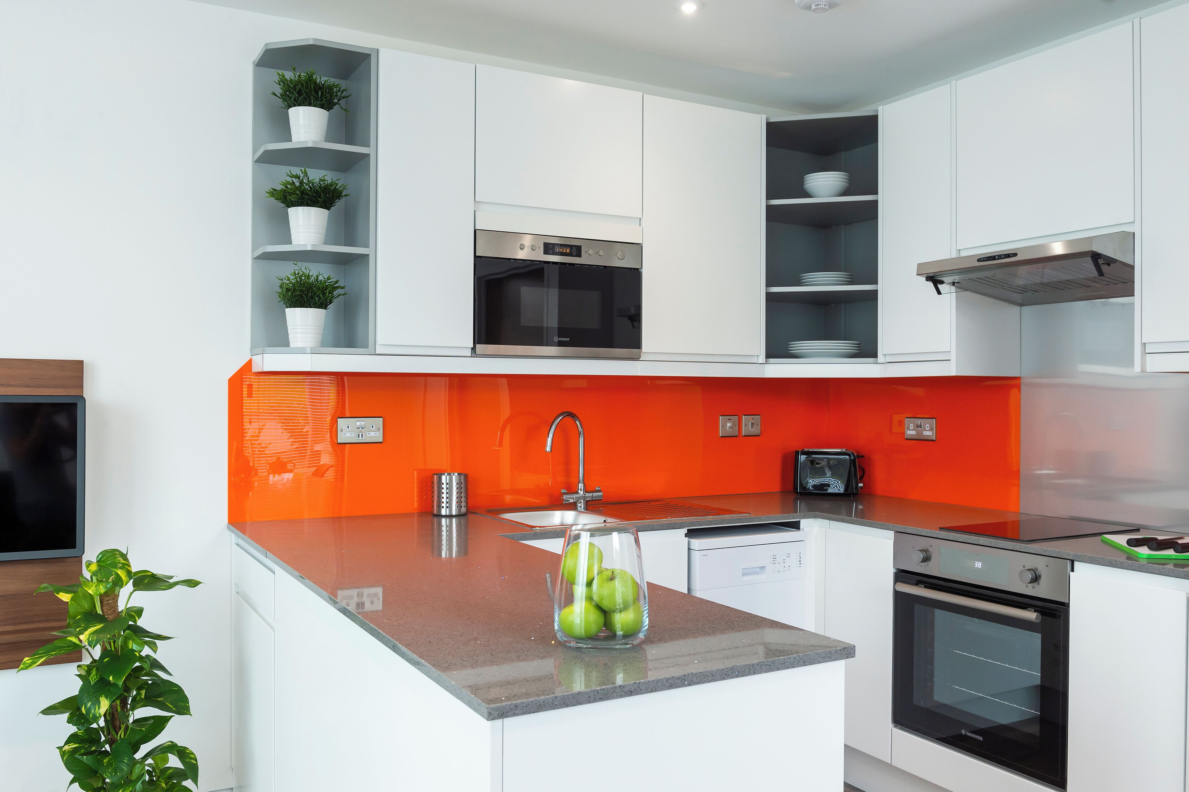 A modern kitchen with white cabinetry, a stainless steel oven, and a glass bowl with apples on the counter.