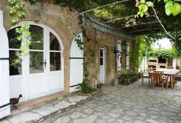 A stone building with arched windows and a covered patio area with a table and chairs.