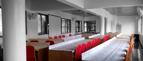 Une salle de conférence avec de longues tables, des chaises rouges et de grandes fenêtres.
