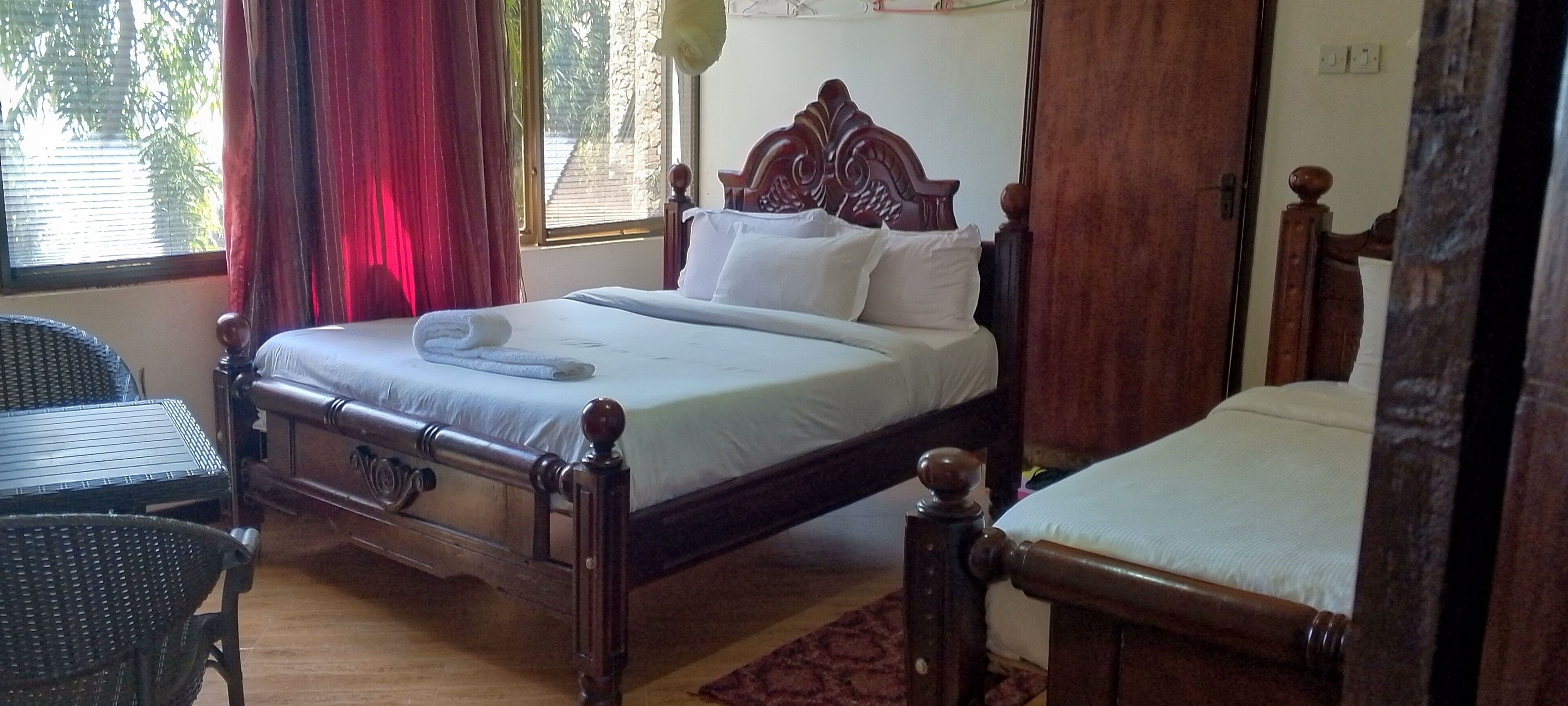 Una cama con dosel de madera con sábanas blancas, una mesita de noche de madera y una silla de mimbre.