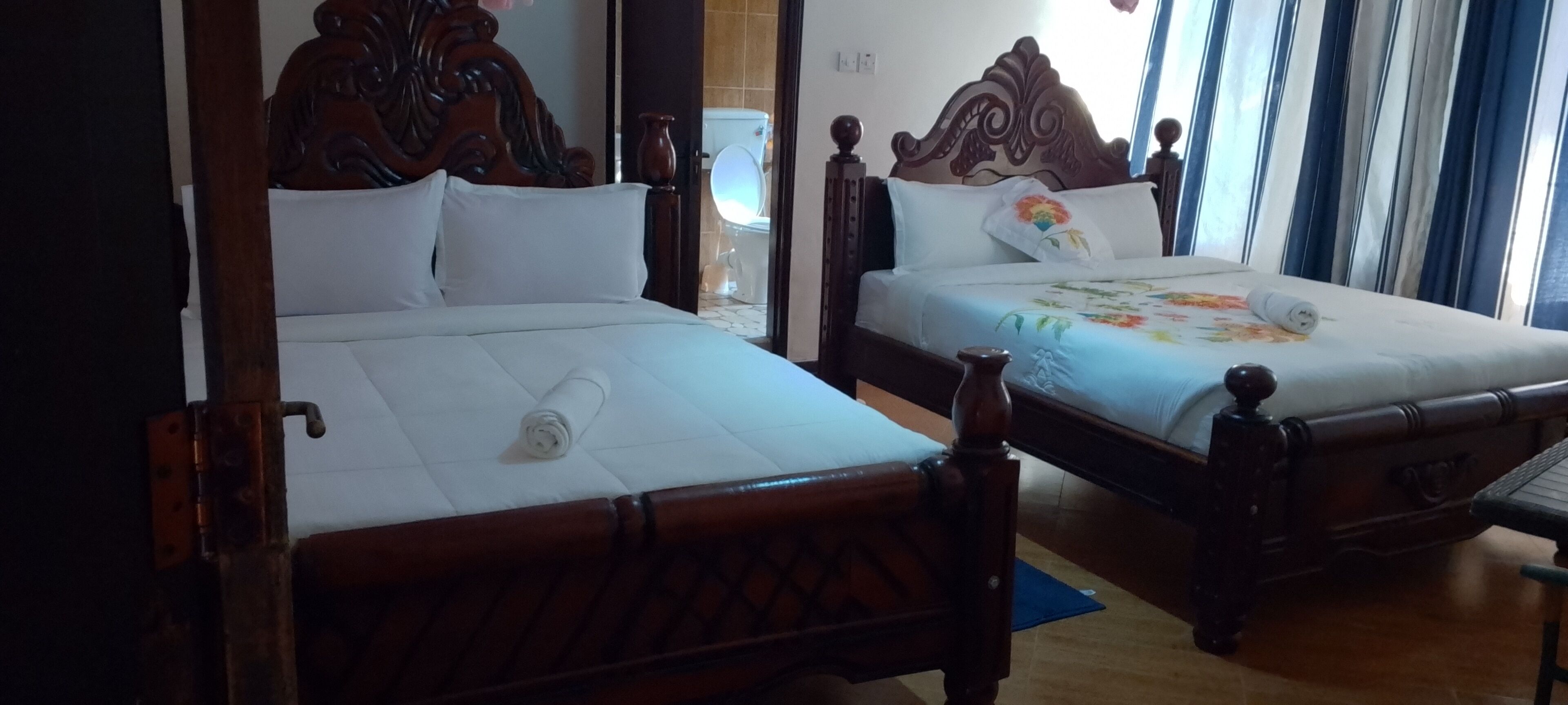 Two wooden beds with white linens, a wooden headboard, and a blue mat on the floor.