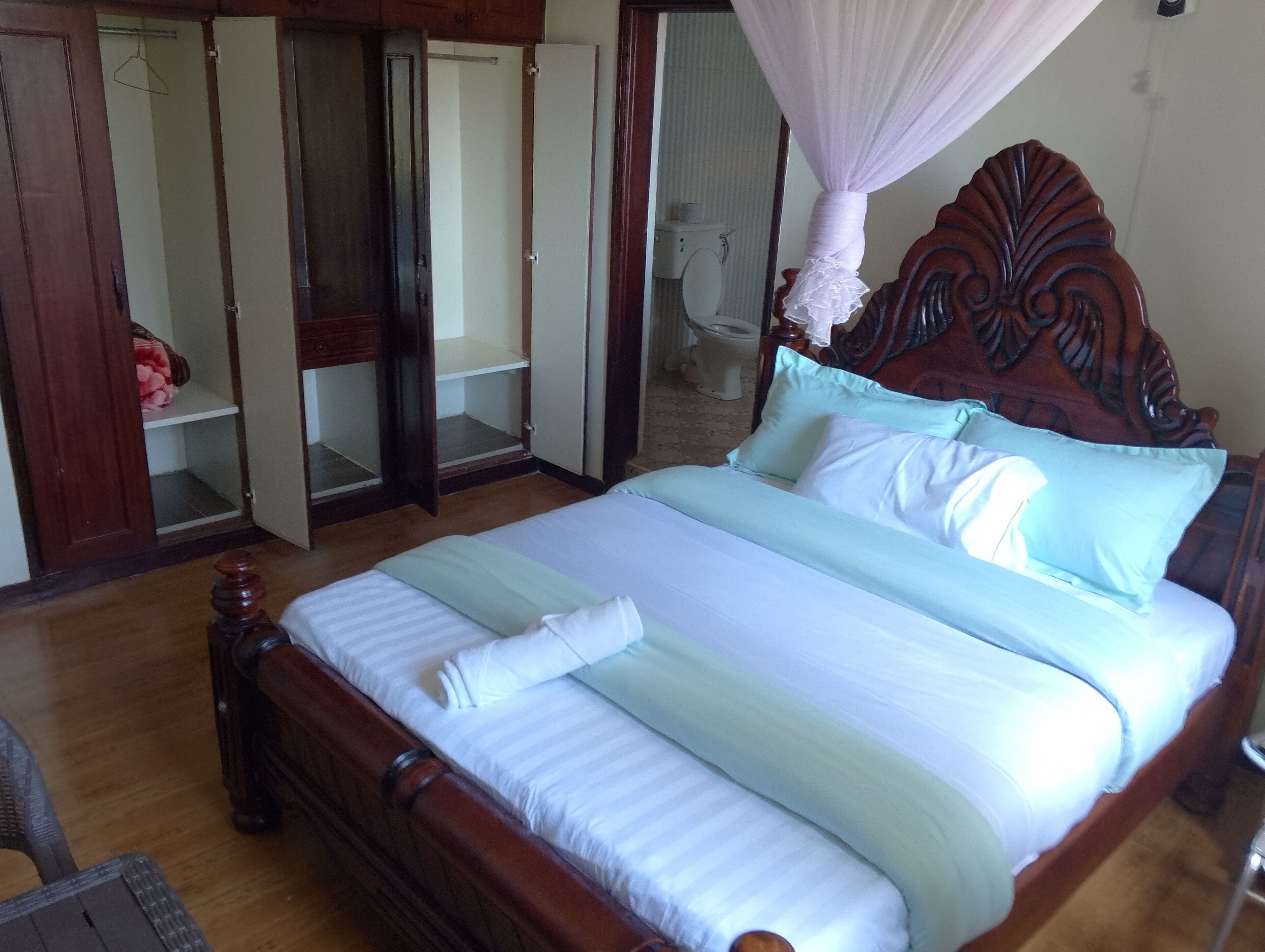 Een slaapkamer met een houten bed, witte beddengoed, een hemelbed en een kledingkast met schuifdeuren.