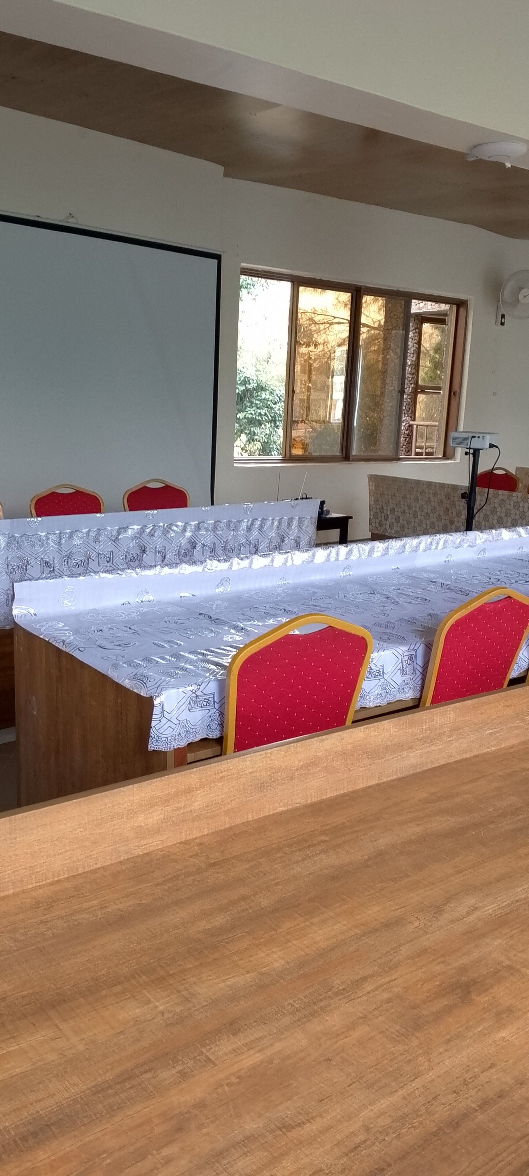 A conference room with a long table, red chairs, a white tablecloth, and a window with a view of trees.