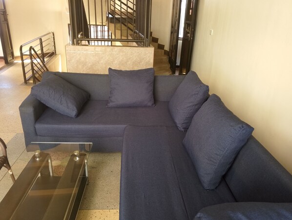 Um sofá modular cinza escuro com almofadas combinando, uma mesa de centro de vidro e uma cadeira de metal.