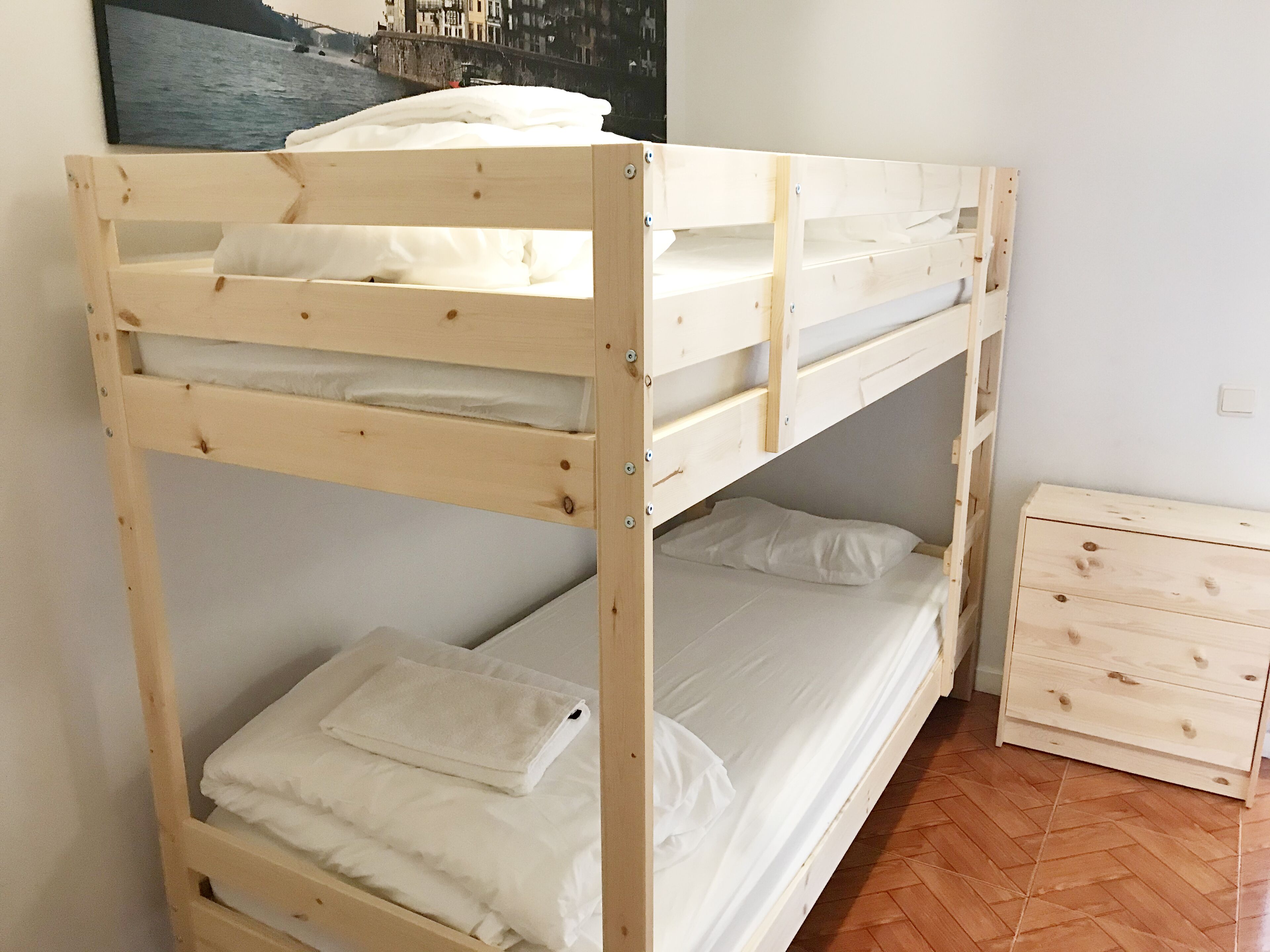 Una cama litera de dos plazas, un aparador de madera y un cartel en la pared.