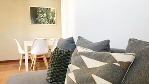 A modern living room with a grey sofa, patterned cushions, a dining table with white chairs, and a framed artwork on the wall. - Clérigos Apartments (Porto)