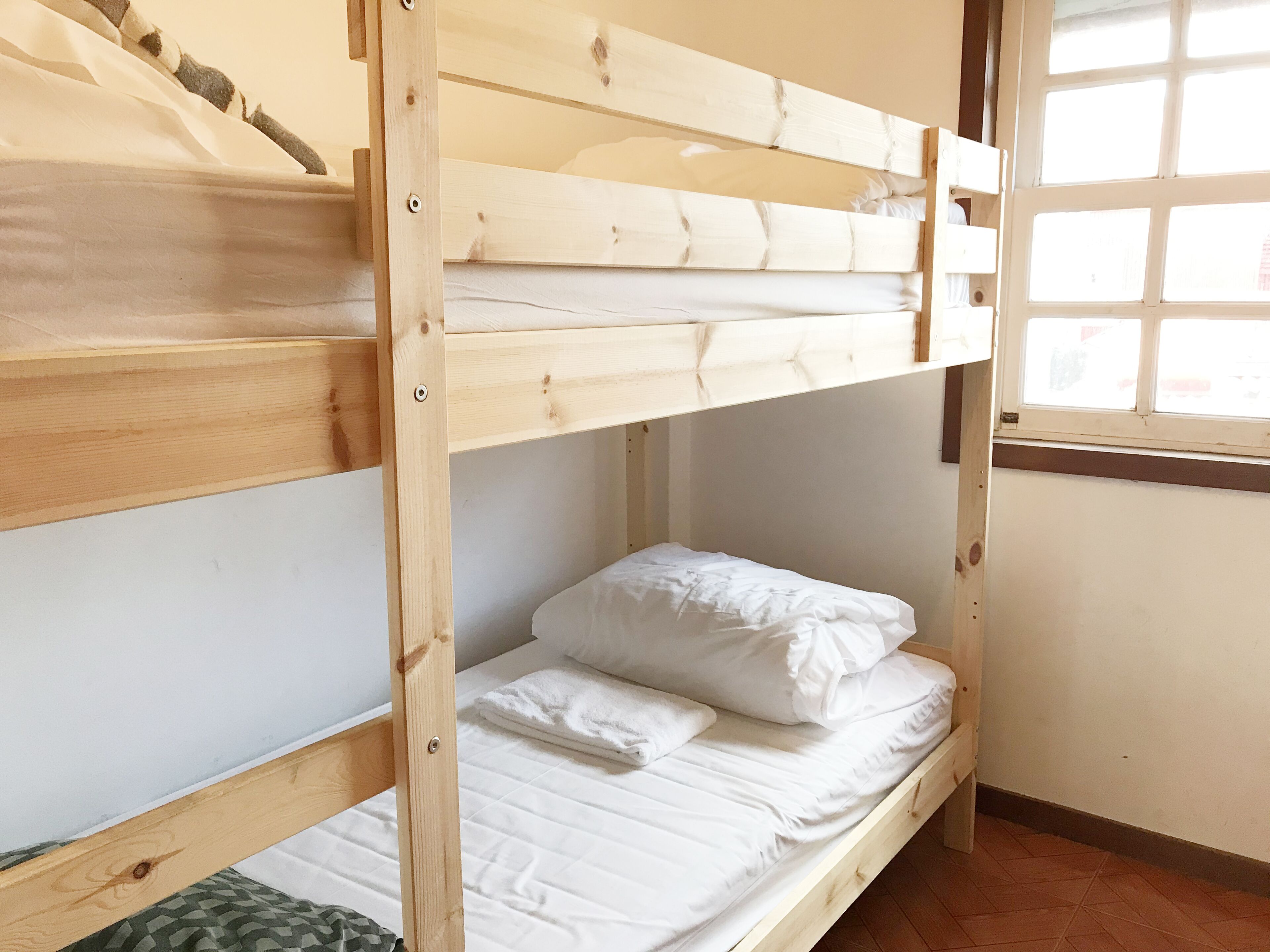 A bunk bed with white bedding and a window with a grid pattern.