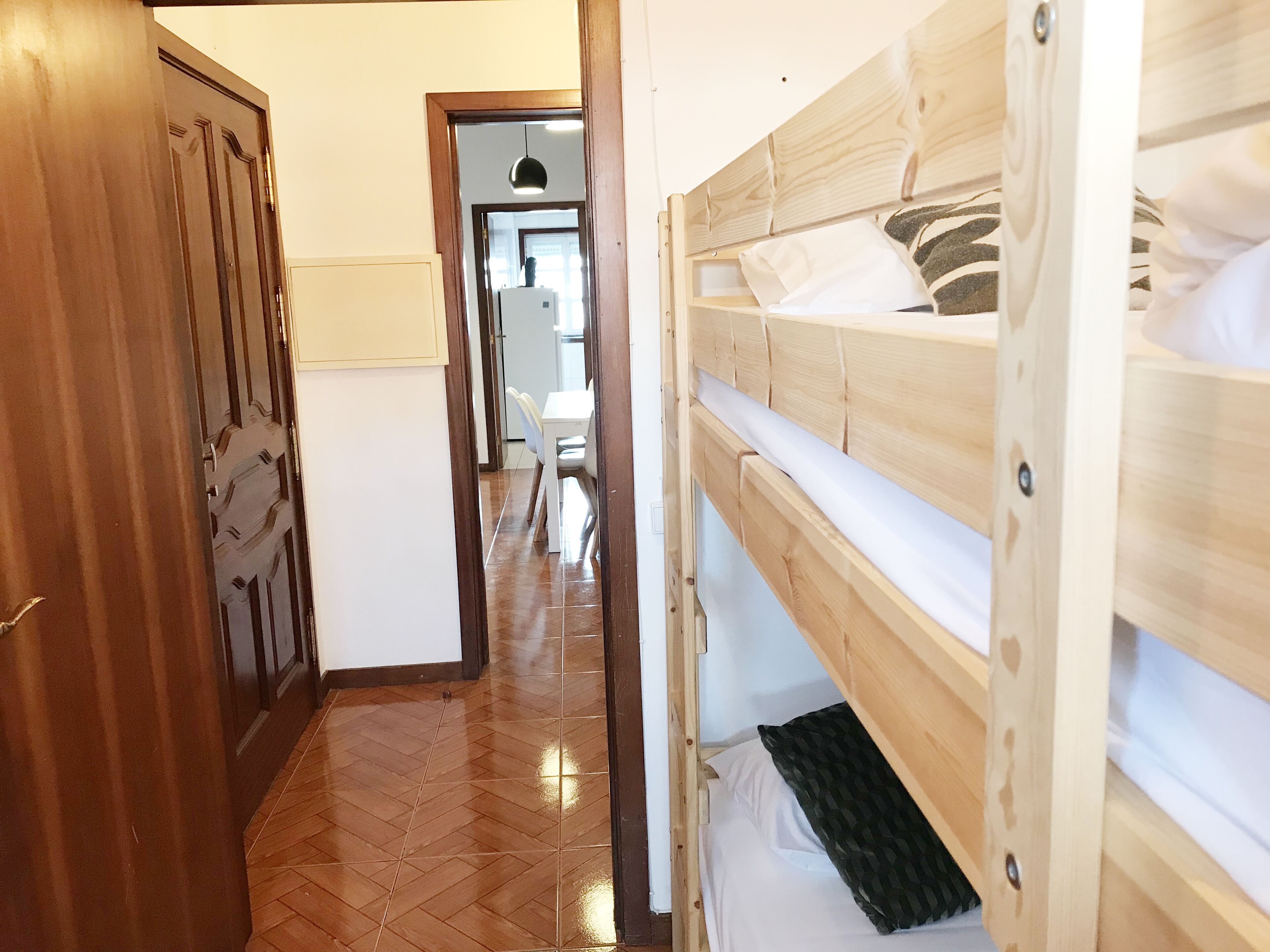 Un pasillo estrecho con puertas de madera y una cama litera con ropa de cama blanca.