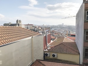 A rooftop with a tiled roof, a building with a white facade, and a view of a cityscape in the background. - Clérigos Apartments (Porto)