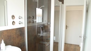 Un baño moderno con cabina de ducha de vidrio, un lavabo blanco y un espejo grande.