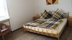 Un dormitorio con estructura metálica para la cama, una silla de madera, una mesita de noche y una pared decorada con dos cuadros con forma de corazón.