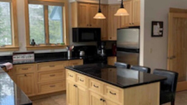 Een moderne keuken met houten kastjes, een zwart aanrecht en hanglampen.
