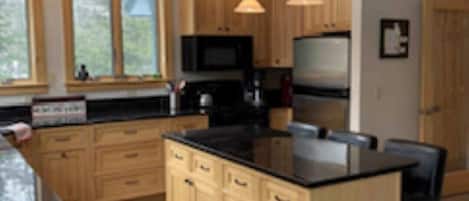 Una cocina moderna con armarios de madera, encimera negra e iluminación colgante.