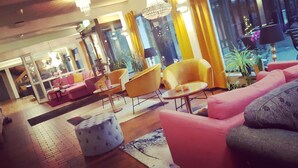 A modern hotel lobby with pink sofas, yellow chairs, and a wooden floor.