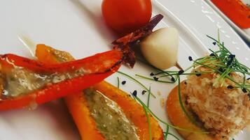 En vit tallrik med ett spett av grillade grönsaker, en körsbärstomat, en liten klick grädde och en bit bröd garnerad med örter.