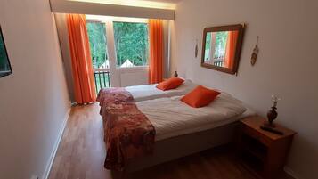 A bedroom with two beds, a wooden nightstand, a mirror, and a window with orange curtains.