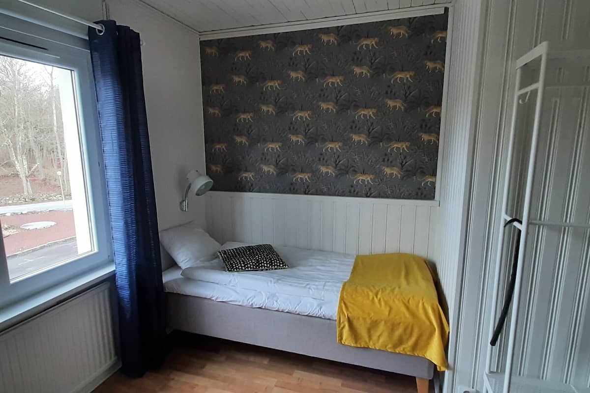 A single bed with a white mattress, a yellow blanket, and a patterned headboard.