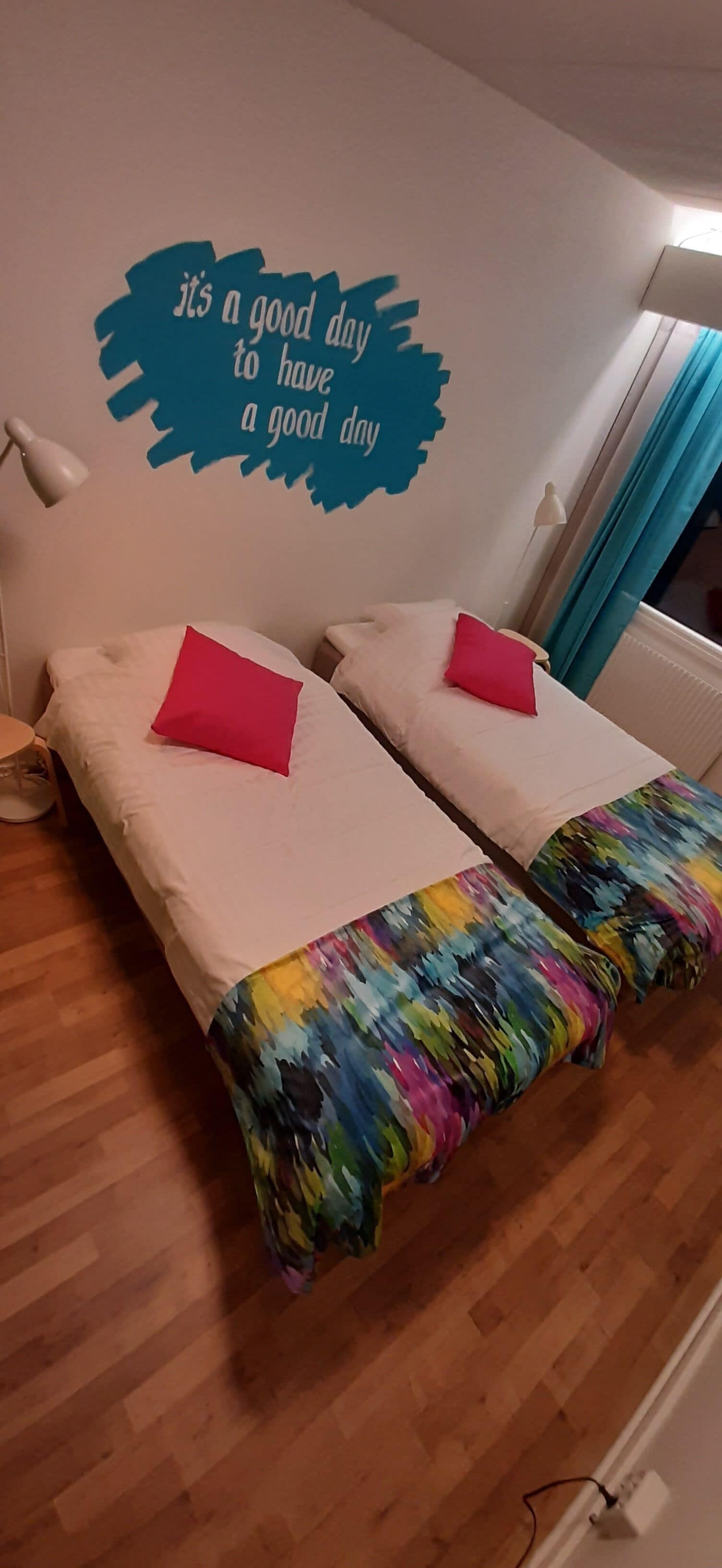 A room with two beds, each with a red pillow, and a wall decal saying "it's a good day to have a good day".