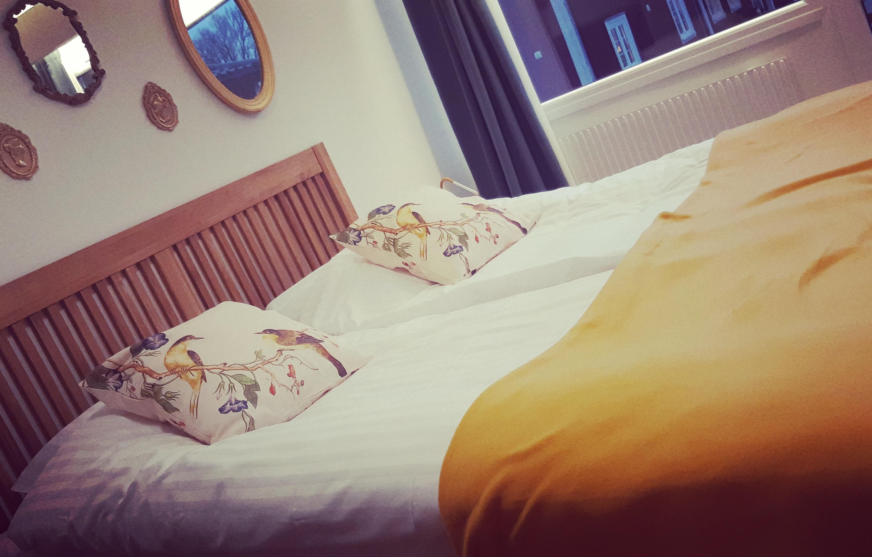 A bed with two pillows, a wooden headboard, and a window with curtains.