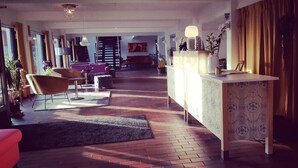 A spacious living area with a wooden floor, a sofa, a coffee table, and a dining table with chairs. There is a staircase leading to another level.