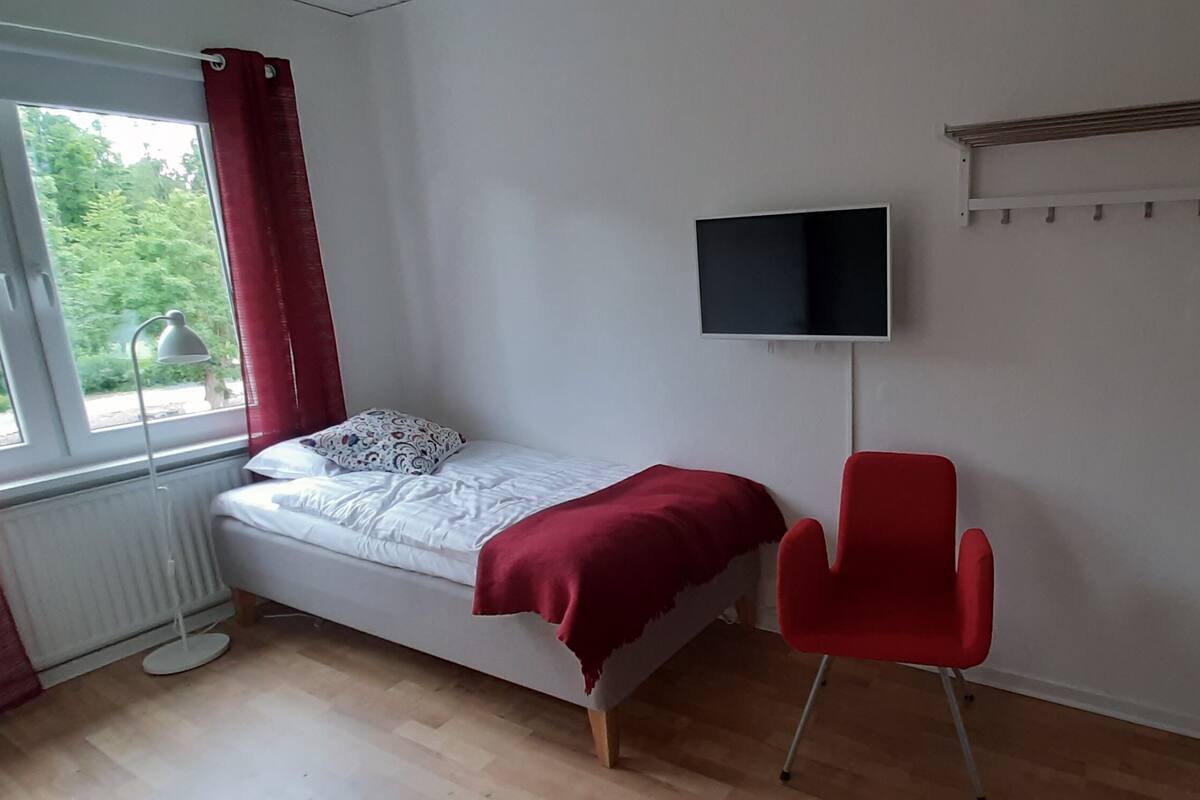 A bedroom with a bed, a red chair, a TV, and a radiator.