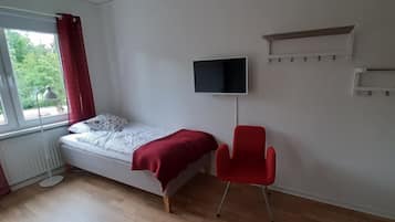 A bedroom with a bed, a red chair, a TV, and a radiator.