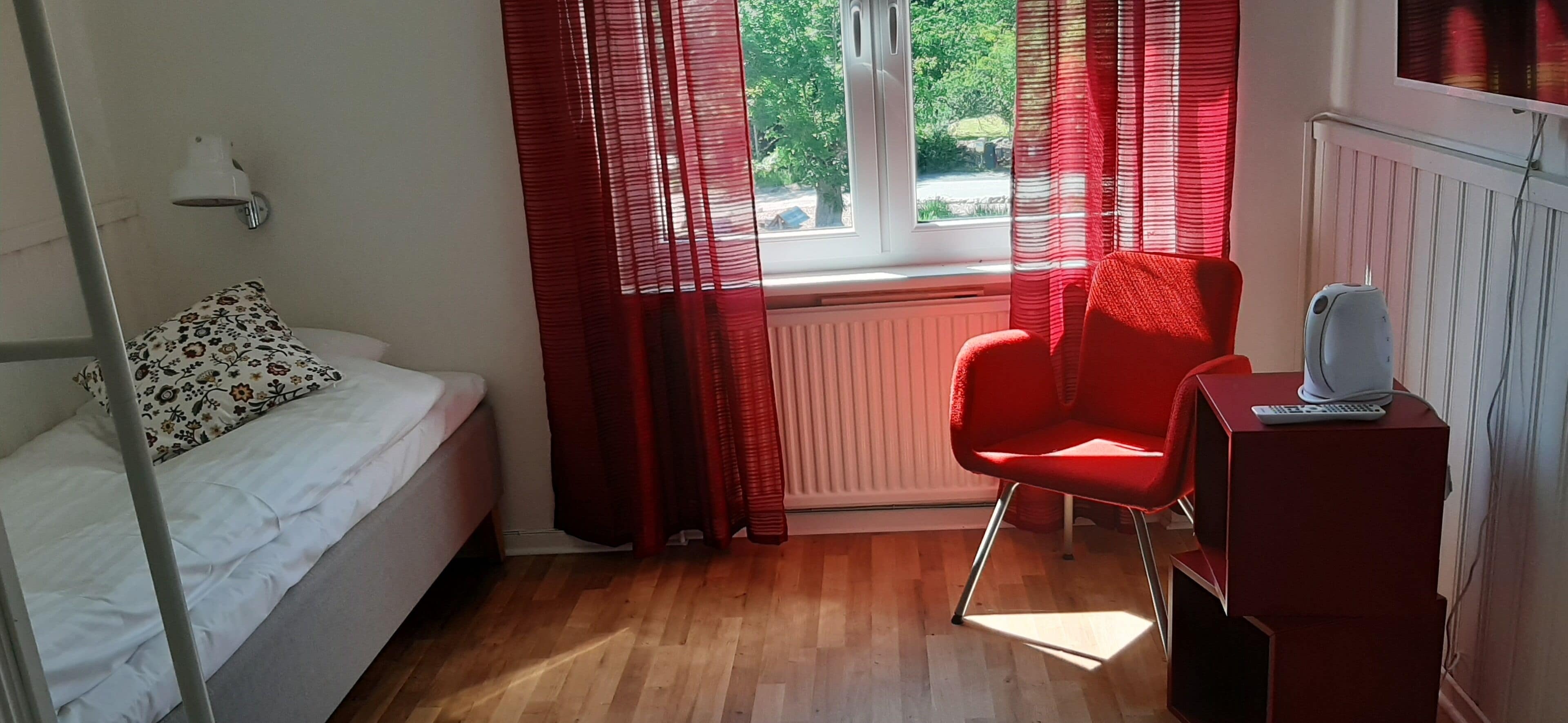 Un dormitorio con una cama, una silla roja, un radiador y una ventana con cortinas.