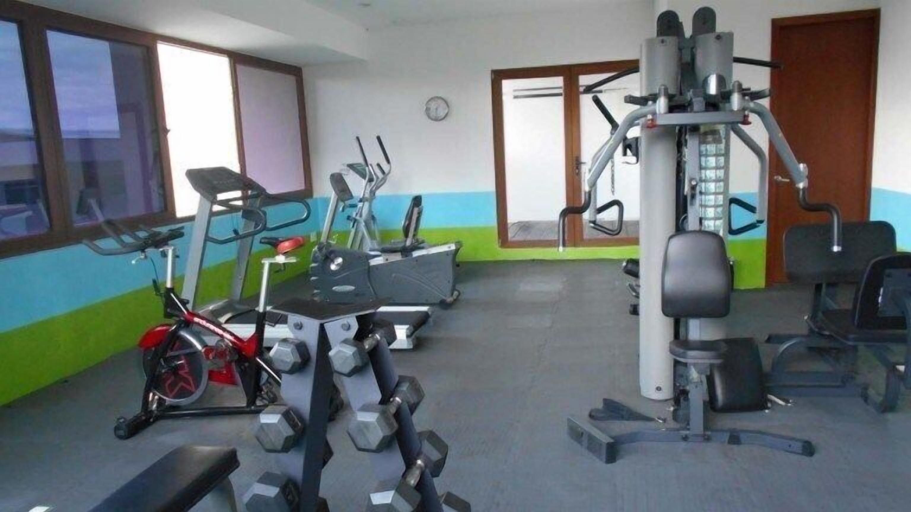 Una palestra con diverse attrezzature per l'allenamento, tra cui tapis roulant, ellittica, cyclette e pesi liberi.